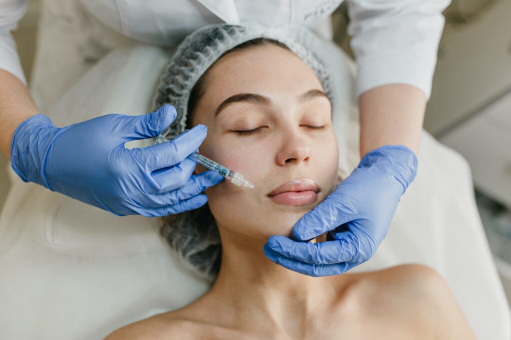 Portrait young woman during cosmetology procedures in beauty salon. Injecting, botox, hands in blue